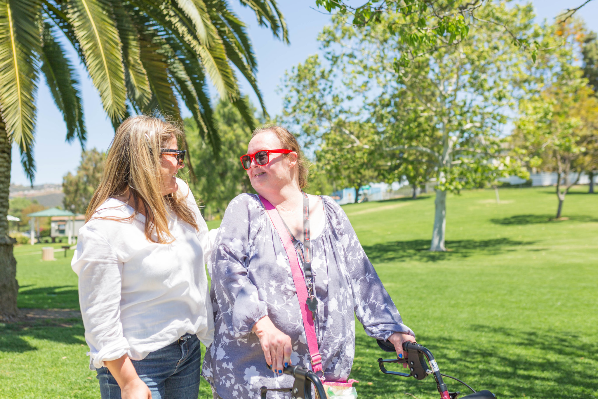 A caregiver and client walk next to each other outside in the park.
